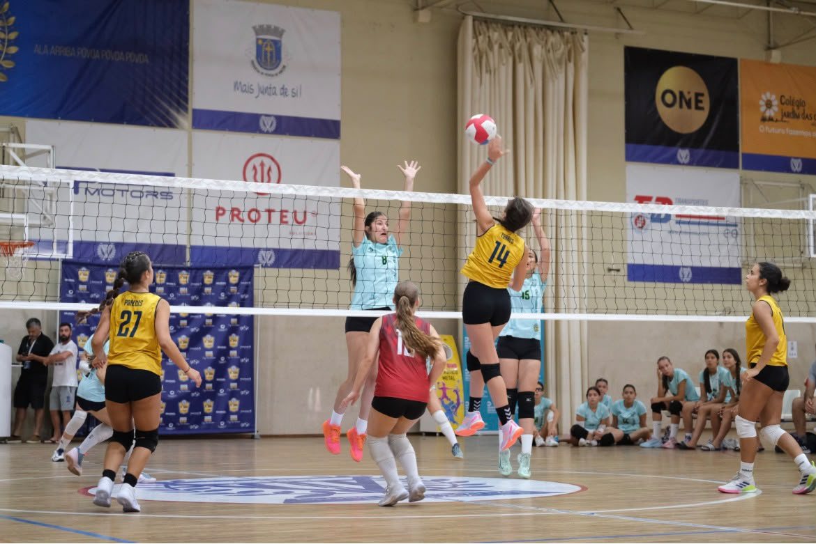 Jogada junto à rede num jogo de voleibol, com uma atleta a atacar e duas adversárias a bloquear